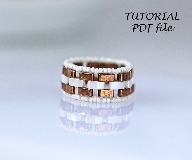 Peut inclure: Une bague en perles blanches et cuivre avec un motif g&eacute;om&eacute;trique. La bague est faite de petites perles blanches et de carr&eacute;s en cuivre. Tutoriel PDF.