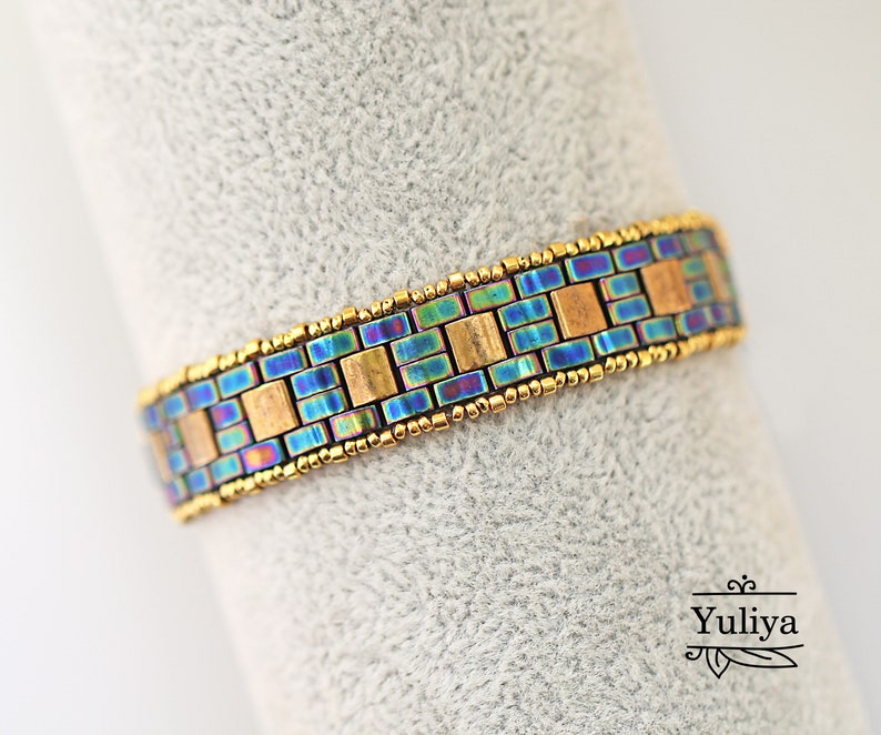 May include: A gold and iridescent blue beaded bracelet with a geometric pattern. The bracelet is made with small square beads.