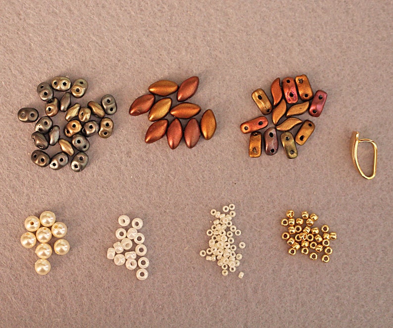 May include: Assortment of beads in various colors and shapes, including gold, brown, white, and gray. There are also pearl-like beads and a gold earring finding.