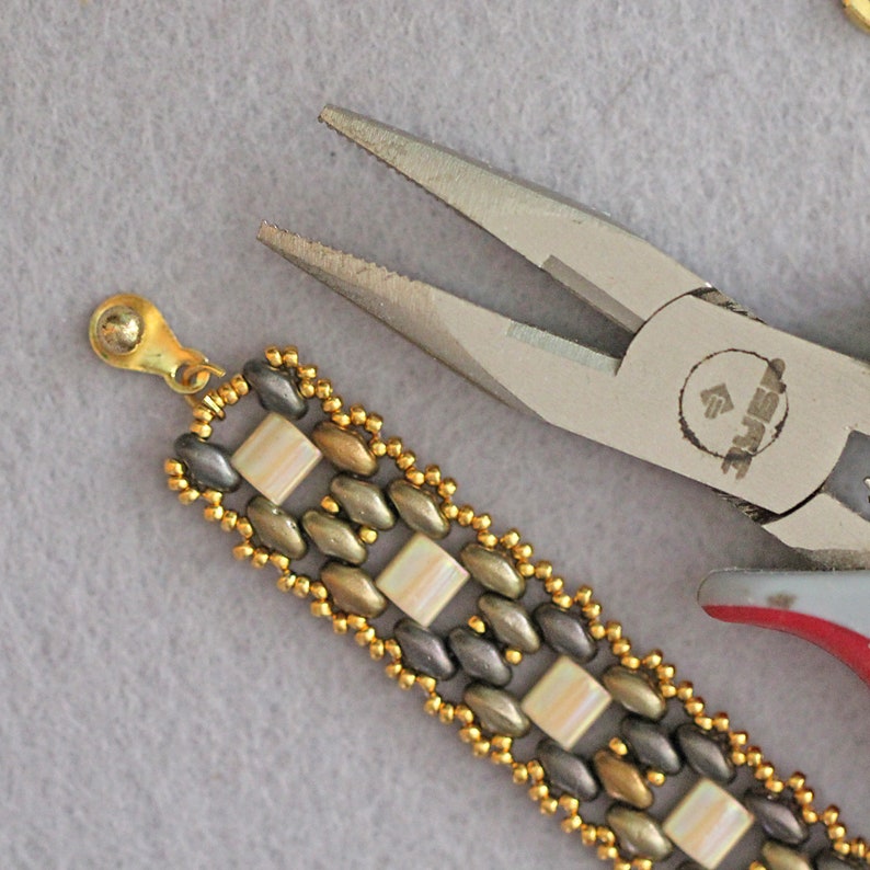 Puede incluir: Primer plano de un brazalete de cuentas doradas y plateadas con un cierre. El brazalete est&aacute; siendo sujetado por un par de alicates plateados con la palabra "Jewel" impresa en el lateral.