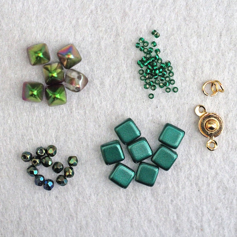 May include: Assortment of green and iridescent glass beads, including round, square, and teardrop shapes. Also included are gold-toned metal clasps and jump rings.