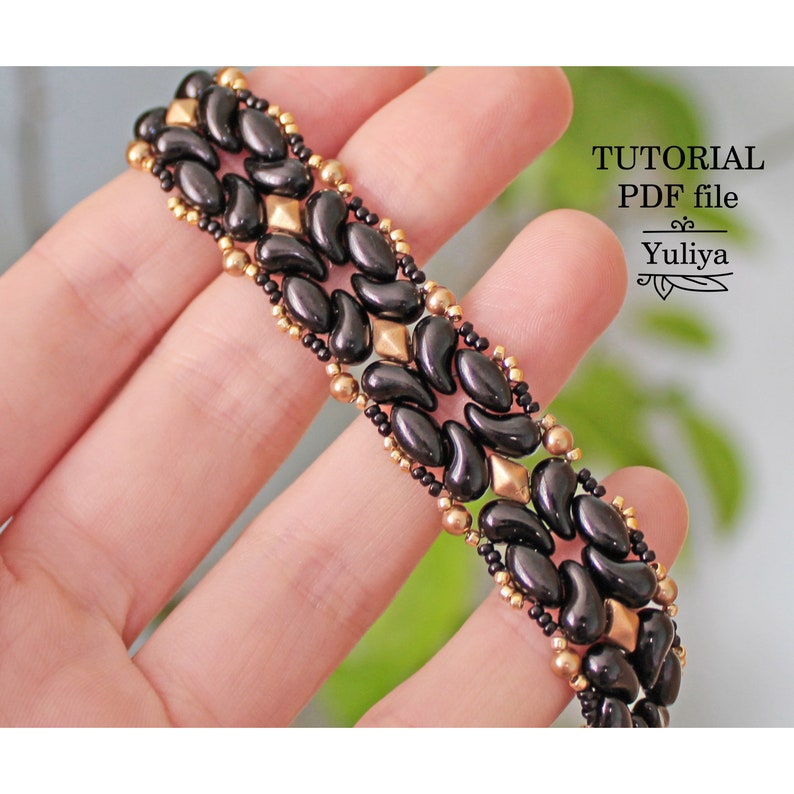 Peut inclure: Un bracelet en perles noires et dor&eacute;es avec un motif en forme de larme. Le bracelet est compos&eacute; de petites perles noires et dor&eacute;es. Le bracelet est pr&eacute;sent&eacute; sur une main.