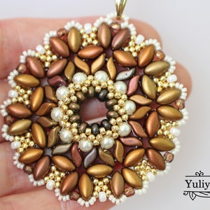 May include: A gold, brown, and white beaded pendant in the shape of a flower. The pendant has a hole in the center and is made with seed beads and pearls.