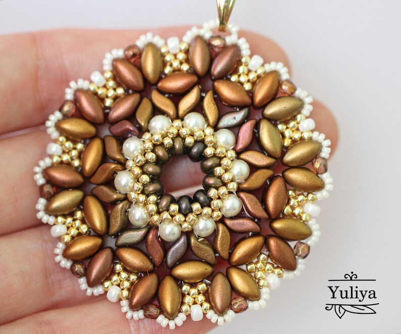 May include: A gold, brown, and white beaded pendant in the shape of a flower. The pendant has a hole in the center and is made with seed beads and pearls.
