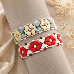 Peut inclure: Deux bracelets en perles avec des perles en forme de goutte. Le bracelet supérieur présente des perles crème et bleu clair avec des perles de rocaille argentées. Le bracelet inférieur a des perles rouges et blanches avec de petites perles de rocaille.