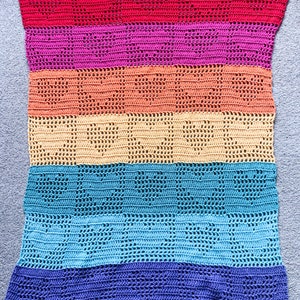 May include: A multi-colored crocheted blanket with a rainbow pattern. The blanket is made with a variety of colors, including red, pink, orange, yellow, blue, and purple.