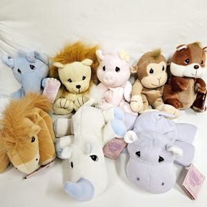 May include: A collection of plush animal toys, including a blue elephant, a lion, a pink pig, a monkey, a brown bear, a tan horse, a white unicorn, and a lavender cow. Each toy has a tag attached.