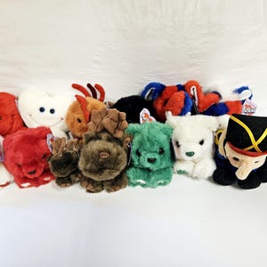 May include: A collection of 12 plush toys, including a red reindeer, a green bear, a brown moose, a white polar bear, a white bunny, a red heart, a blue and red penguin, a black and red nutcracker, and a white heart. The toys are all soft and cuddly and have a variety of different expressions.