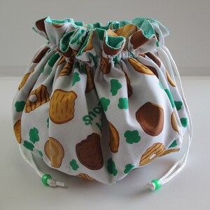 May include: White drawstring bag with a green and white print of Girl Scout cookies. The bag has a white drawstring with green beads.