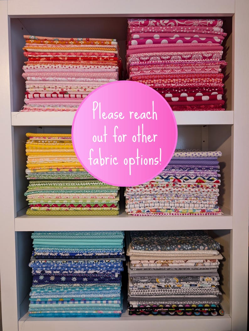 May include: A white shelf unit with multiple stacks of colorful fabric. The fabric is patterned with various designs, including polka dots, stripes, and floral prints. A pink circle with the text "Please reach out for other fabric options!" is placed in front of the shelf unit.