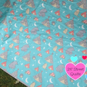May include: A turquoise blue baby quilt with a repeating pattern of gray bears, red and white tents, and stars. The quilt has a gray border and the text "24th Street Quilts" in pink.