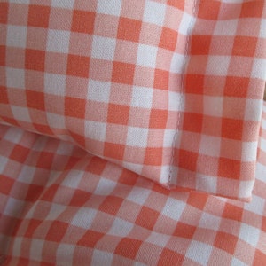 May include: Two orange and white gingham pillowcases. The pillowcases are made of a soft, cotton fabric and have a subtle sheen.
