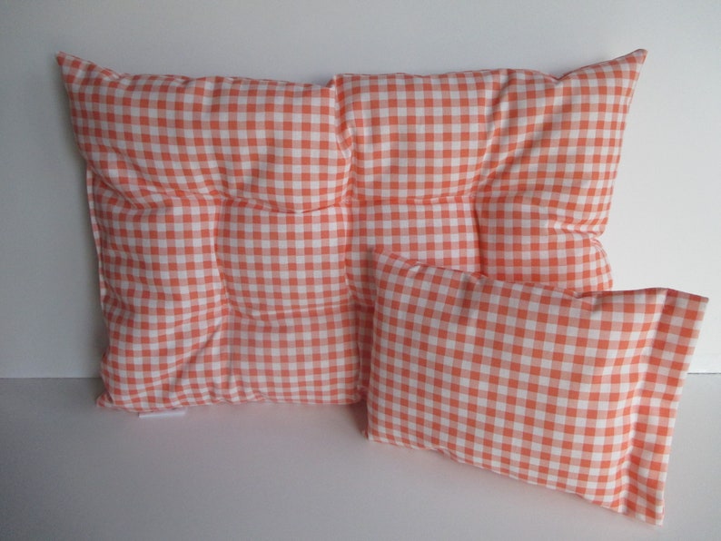 May include: Two orange and white gingham patterned pillows. The larger pillow is square and has a tufted design. The smaller pillow is rectangular.