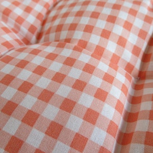 May include: Close-up of a pink and white gingham fabric. The fabric has a checkered pattern with small squares.