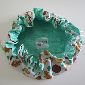 May include: A white drawstring bag with a green lining and a print of brown cookies and green shamrocks. The bag has a label that says "24th Street Quilts".