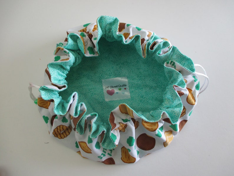 May include: A white drawstring bag with a green lining and a print of brown cookies and green shamrocks. The bag has a label that says "24th Street Quilts".