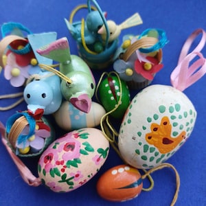 Op de afbeelding: Een verzameling houten paaseieren, waaronder eieren, vogels en manden, versierd met kleurrijke bloemen- en geometrische patronen. De ornamenten zijn geschilderd in tinten blauw, groen, roze, oranje en geel.
