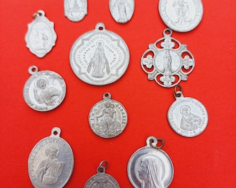 May include: A collection of 11 silver-toned religious medallions with various images and text. The medallions are arranged on a red background.