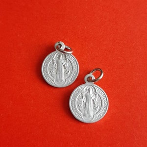 May include: Two silver Saint Christopher medallions with a loop for hanging. The medallions feature a depiction of Saint Christopher carrying a child on his shoulders.