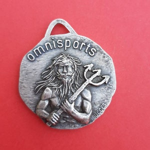 May include: Silver-toned metal keychain with a raised image of a man holding a trident. The keychain is round and has the word "omnisports" written around the top edge. The word "succes" is written on the bottom edge.