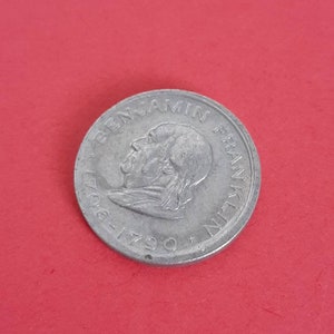 May include: A silver coin featuring a portrait of Benjamin Franklin with the inscription "BENJAMIN FRANKLIN 1706-1790" around the edge.