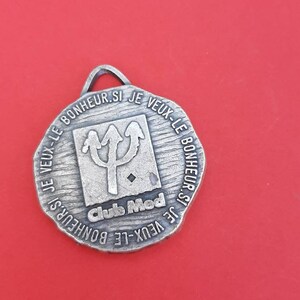 May include: Silver-toned metal keychain with a trident logo and the text "Club Med" and the phrase "Je veux le bonheur si je veux le bonheur".