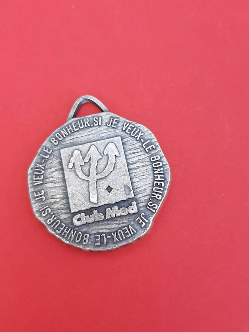 May include: Silver-toned metal keychain with a trident logo and the text "Club Med" and the phrase "Je veux le bonheur si je veux le bonheur".