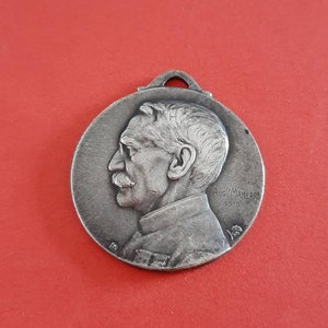 May include: Silver medal with a profile portrait of a man with a mustache and the text "Aug. M. Maillard 1915".