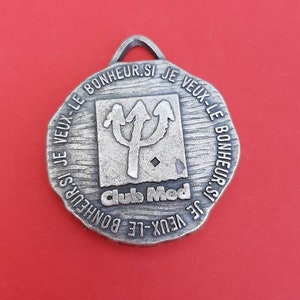 May include: A silver-toned metal keychain with a circular design. The keychain features a trident symbol and the text "IF VEUX-LE BONHEUR.SI JE VEUX-LE BONHEUR.SI JE VEUX-LE BONHEUR SI Clubs Med".