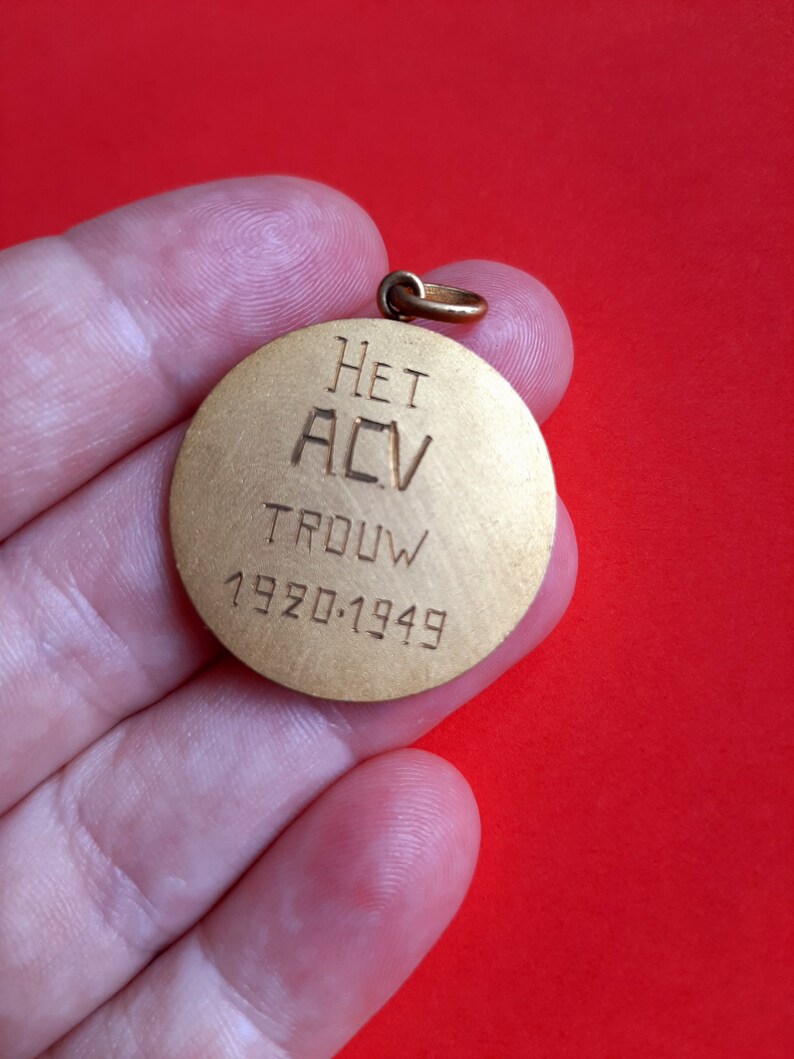 May include: A gold-colored round medal with the text "HET ACV TROUW 1920-1949" engraved on it.