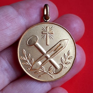 May include: Gold-toned pendant with a cross, two nails, and a laurel wreath design.