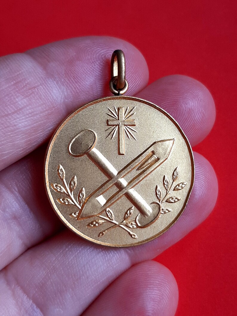 May include: Gold-toned pendant with a cross, two nails, and a laurel wreath design.