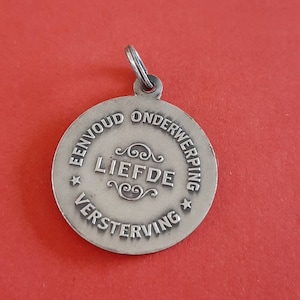 May include: Silver pendant with the inscription "Eenvoud Onderwerping Liefde Versterving" in Dutch.