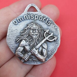 May include: Silver-toned metal keychain with a raised image of a man holding a trident. The keychain is round and has the words "omnisports" and "succes" inscribed on it.