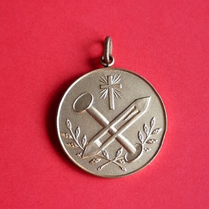 May include: A gold-toned pendant with a cross and two nails, surrounded by a wreath of leaves.