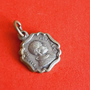 Op de afbeelding: Zilverkleurige hanger met een profiel van een persoon met de tekst "PONT. MAX." en "P.P.I.S." rond de rand.