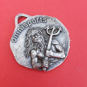 May include: Silver-toned metal keychain with a raised image of a man holding a trident. The text "omnisports" is engraved around the edge of the keychain. The word "succes" is engraved on the side.