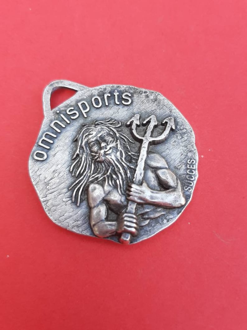 May include: Silver-toned metal keychain with a raised image of a man holding a trident. The text "omnisports" is engraved around the edge of the keychain. The word "succes" is engraved on the side.