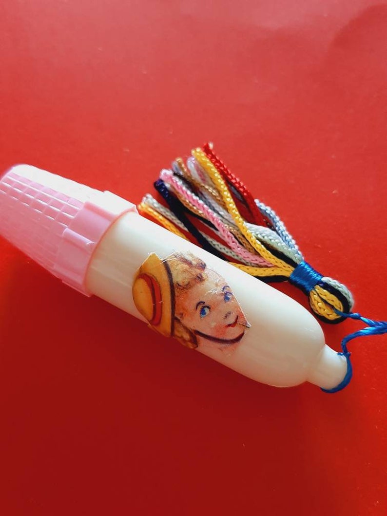 Pu&ograve; includere: Un ditale di plastica bianca con un tappo rosa e un fiocco colorato. Il ditale ha un adesivo di un bambino con un cappello.