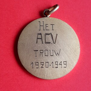 May include: A gold-colored metal pendant with the inscription "HET ACV TROUW 1920.1949".