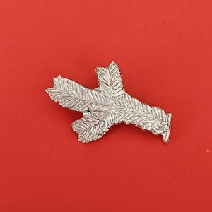 Op de afbeelding: Zilverkleurige metalen broche in de vorm van een gestileerde vogelpoot.
