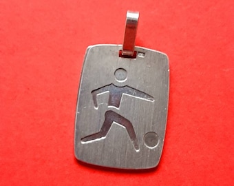 May include: Silver pendant charm featuring a stylized silhouette of a soccer player kicking a ball. The pendant is rectangular with a smooth, brushed finish.