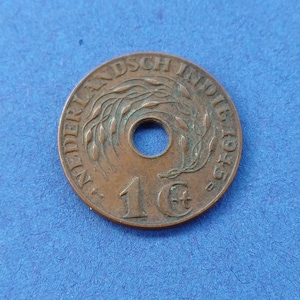 Può includere: Una moneta color bronzo delle Indie Orientali Olandesi, con un foro centrale. La moneta presenta testo sul bordo e il numero "1" con un simbolo "c". L'anno "1945" è visibile sulla moneta.