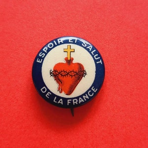 May include: A blue and white button with the text "ESPOIR ET SALUT DE LA FRANCE" surrounding a red heart with a gold cross and thorns.