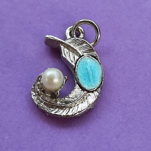 Op de afbeelding: Een zilveren bedel in de vorm van een veer met een blauwe en witte steen. De bedel heeft een lus aan de bovenkant om aan een armband of ketting te bevestigen.