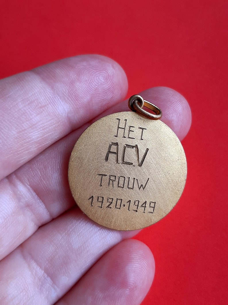 May include: A gold-colored round metal pendant with the inscription "HET ACV TROUW 1920-1949".