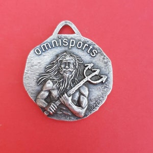May include: Silver-toned metal keychain with a raised image of a man holding a trident. The keychain is round and has the words "omnisports" and "succes" inscribed on it.