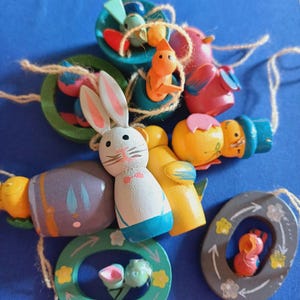 Puede incluir: Una colección de adornos de Pascua de madera coloridos, que incluyen un conejito, un pájaro, un pollito y una corona. Los adornos están pintados en colores brillantes y tienen un aspecto artesanal y caprichoso.