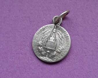 May include: Silver charm with a religious image and the text "Miracle de Bois Seigneur" around the edge.