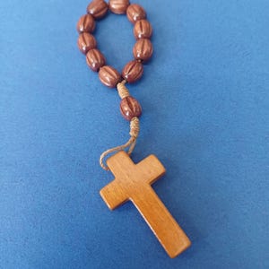 Pu&ograve; includere: Un rosario in legno con grani marroni e una croce. Le perle ovali sono infilate e collegate alla croce da un cordino annodato. La croce ha un design semplice e classico.